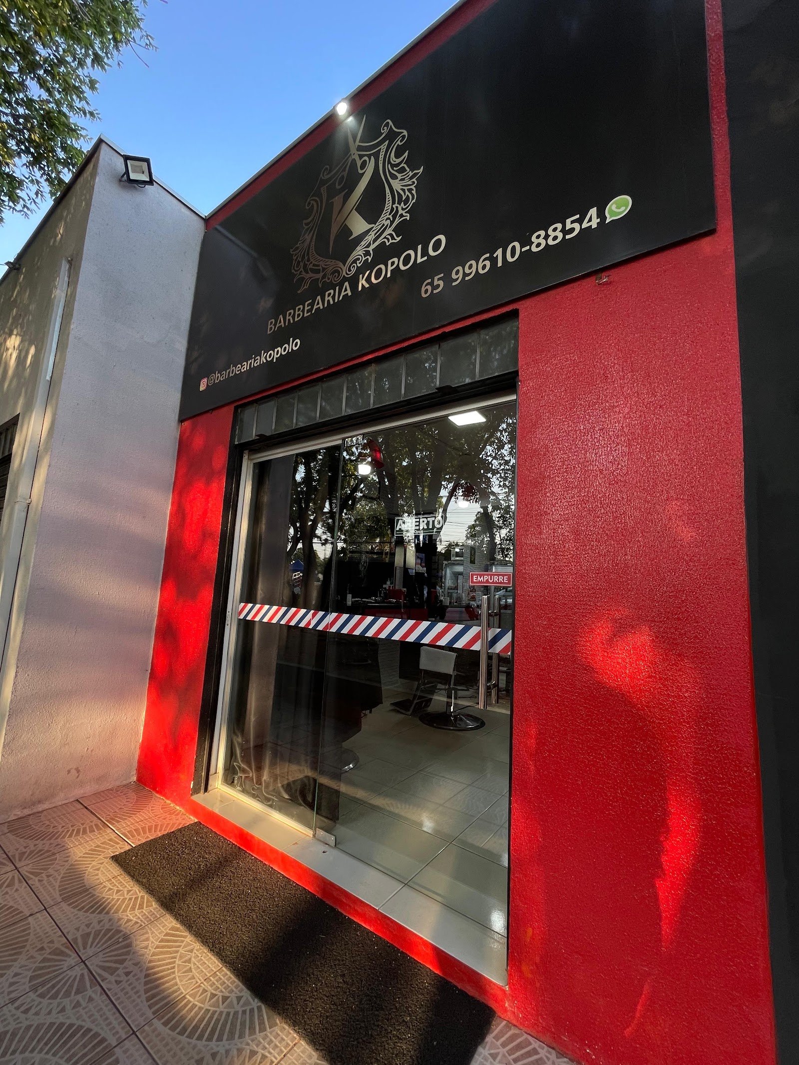 Fachada da Barbearia Kopolo ao entardecer, com letreiro dourado e faixa de poste de barbeiro